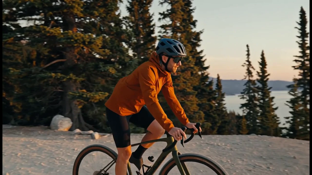 An orange-jacketed cyclist follows a gravel road to a lake overlook. A tracking view, wheel detail and final pause give this 15-second film a beginning, movement and destination.
