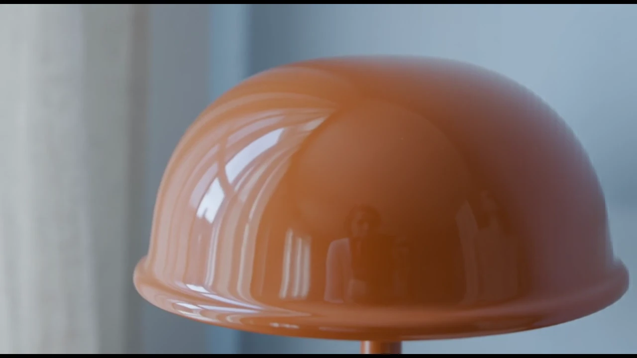 The opening moves close to the orange enamel shade, catching the window reflection before revealing the whole lamp.